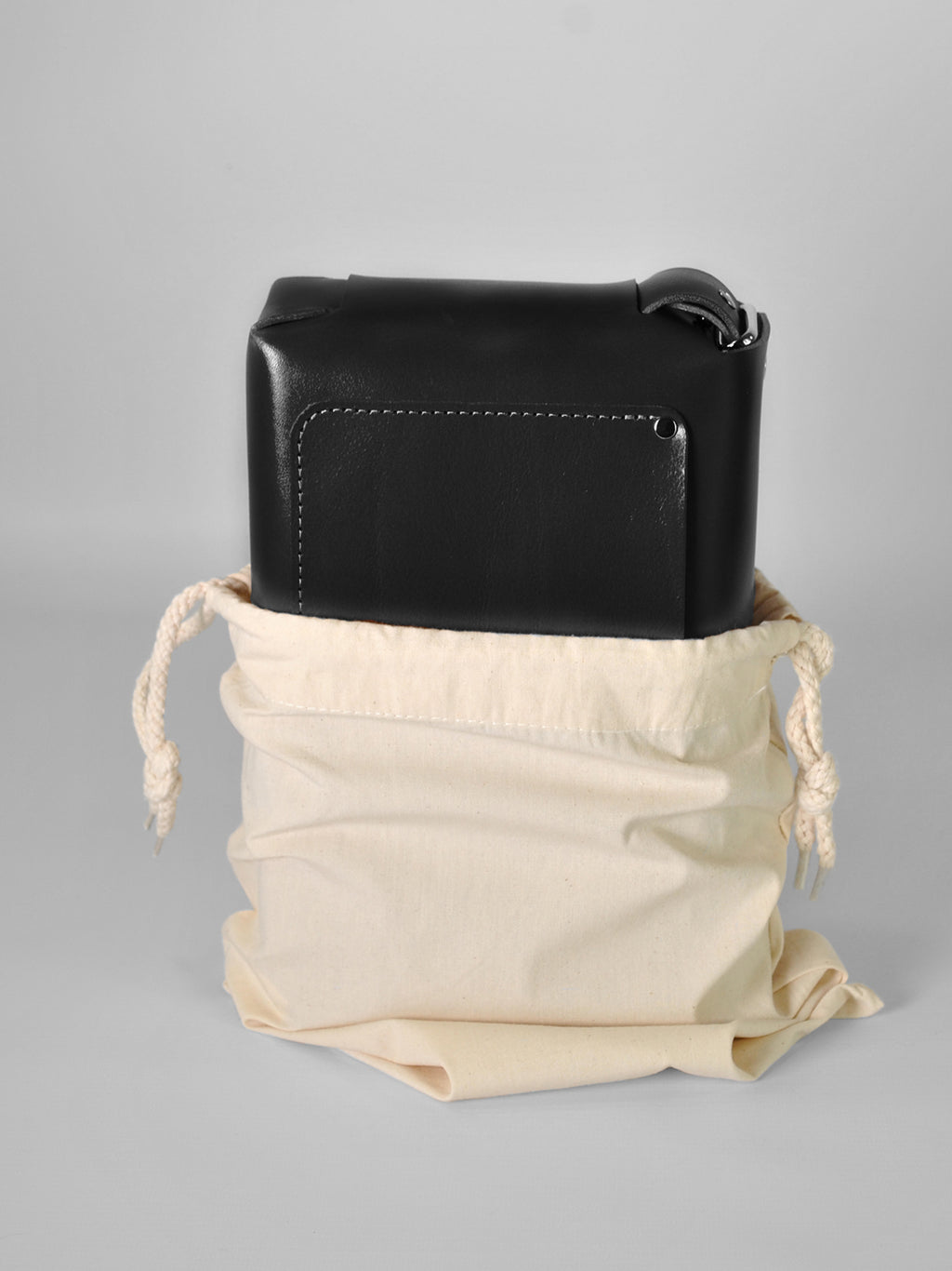 Black leather crossbody bag in a beige drawstring bag for storage 
