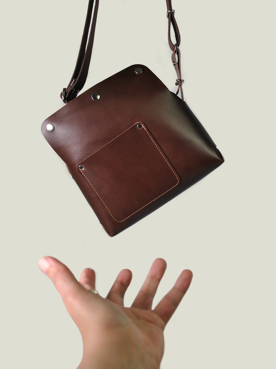 Brown leather handbag held by a hand against a plain background